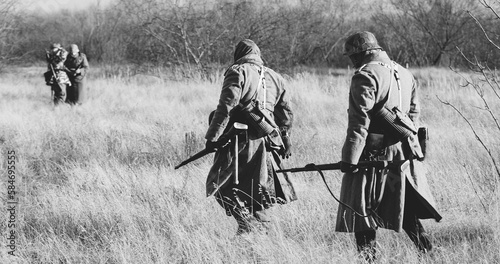 Re-enactors Dressed As German Infantry Soldiers In World War II Marching Walking Along Meadow In Cold Autumn Day. Black And White Colors. photo