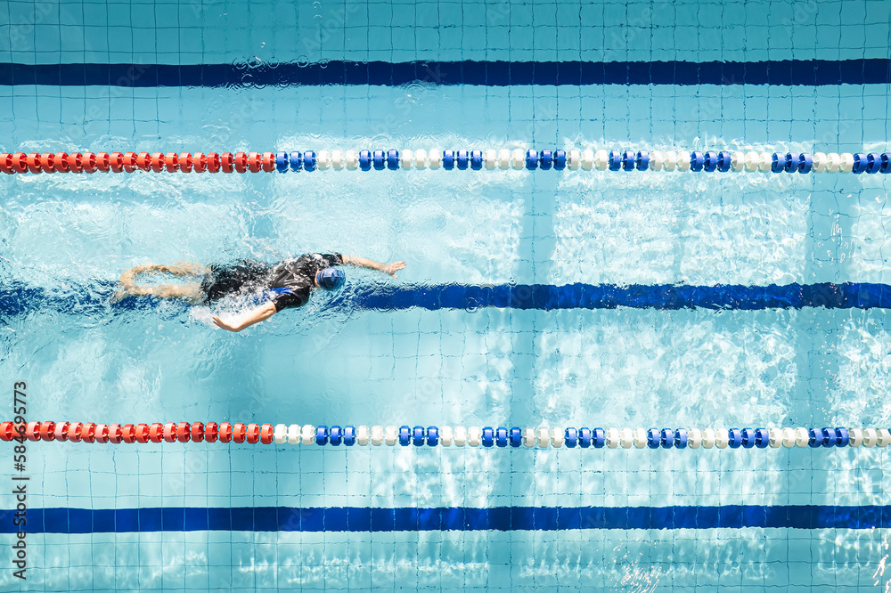 Top view shot of young man swimming laps in a swimming pool. Male swimmer swimming the front crawl in a pool. Swimming pool for sports swimming.