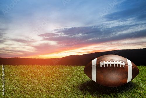 American football ball on green grass field on background of sunset sky. Banner.