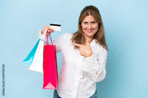 Middle-aged caucasian woman isolated on blue background holding shopping bags and a credit card