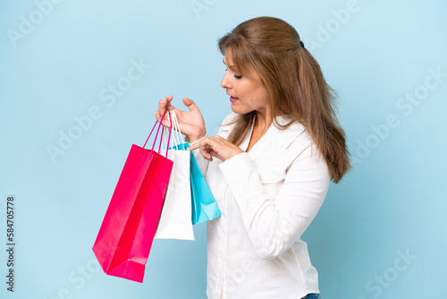 Middle-aged caucasian woman isolated on blue background holding shopping bags