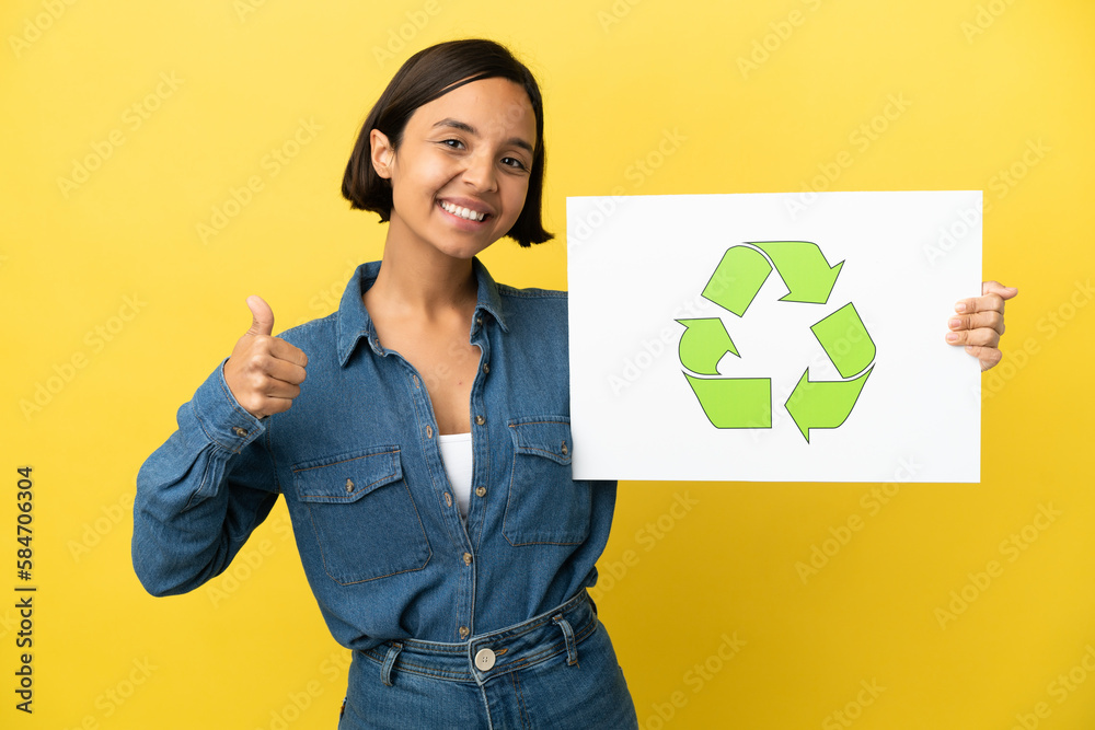 Young mixed race woman isolated on yellow background holding a placard with recycle icon with thumb up Young mixed race woman isolated on yellow background holding a placard with recycle icon with thumb up