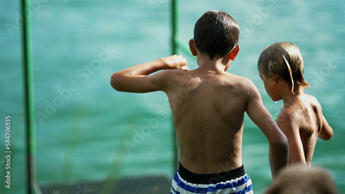Two brothers talking by lake dock pier outdoors. Shirtless wet kids standing outside in nature