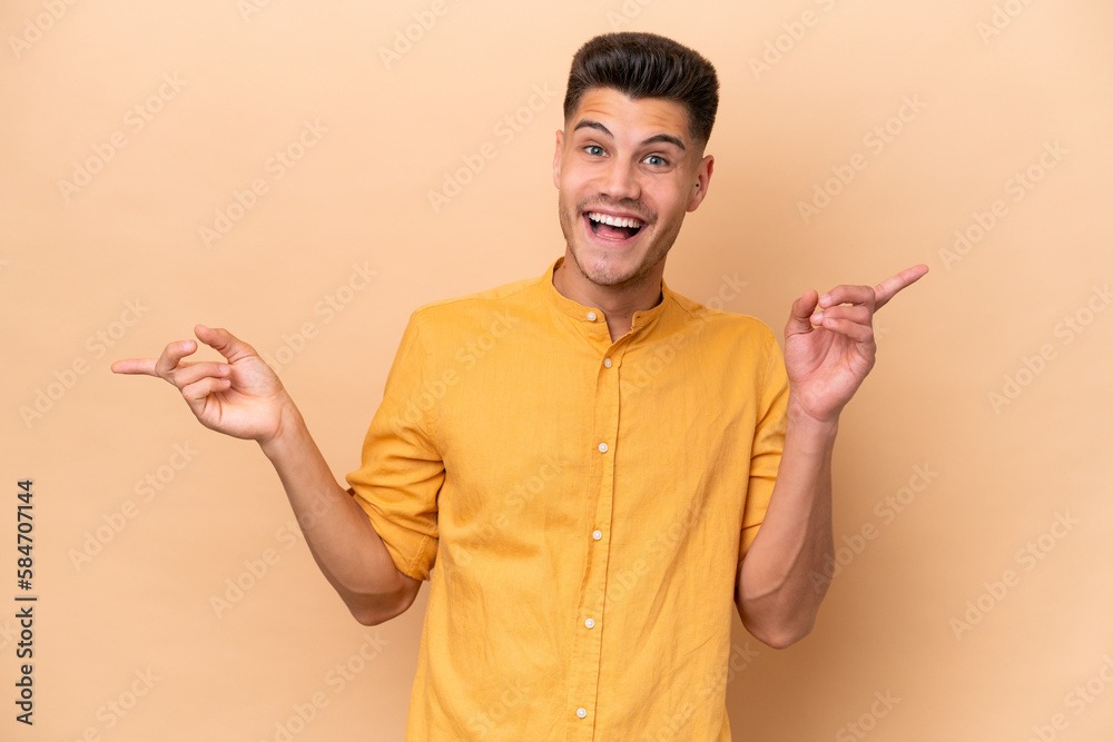 Young caucasian man isolated on beige background pointing finger to the laterals and happy