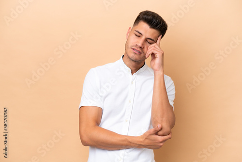 Young caucasian man isolated on beige background with headache