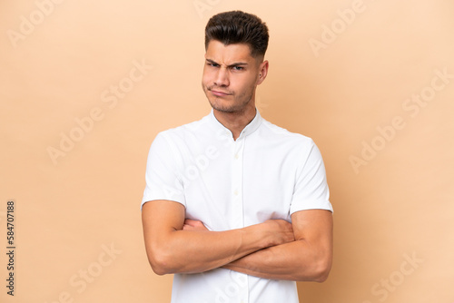 Young caucasian man isolated on beige background feeling upset