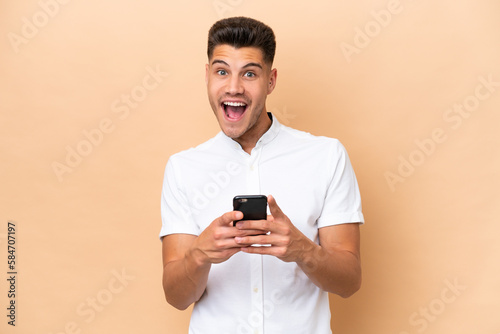 Young caucasian man isolated on beige background surprised and sending a message