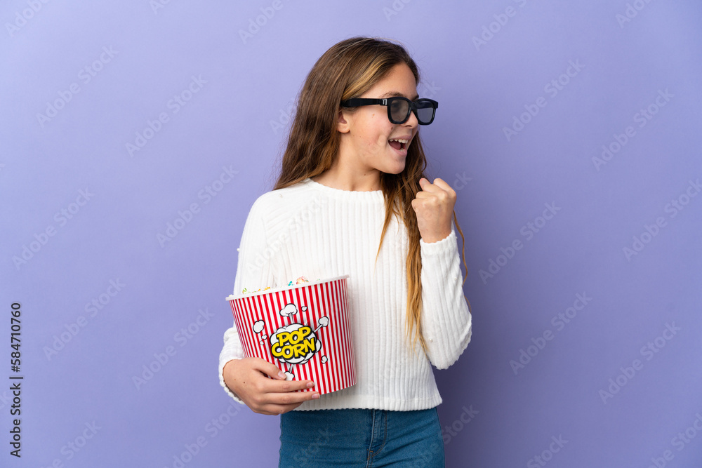 Child over isolated purple background with 3d glasses and holding a big bucket of popcorns while looking side