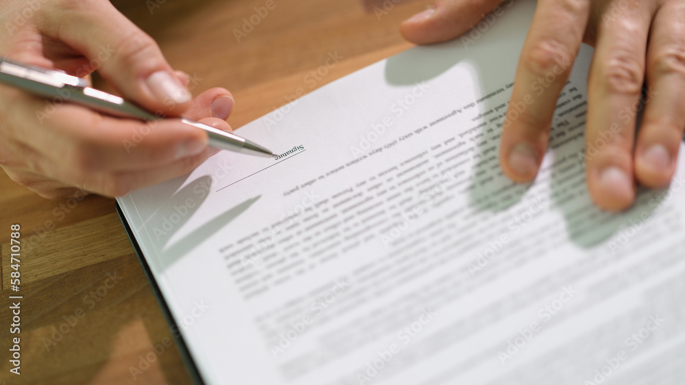 Hands of businessman with pen signing contract document at table closeup Hands of businessman with pen signing contract document at table closeup