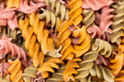 Rice vegetable pasta in the form of spirals, top view. Healthy rice pasta with tomatoes, selenera, carrots and beets photo