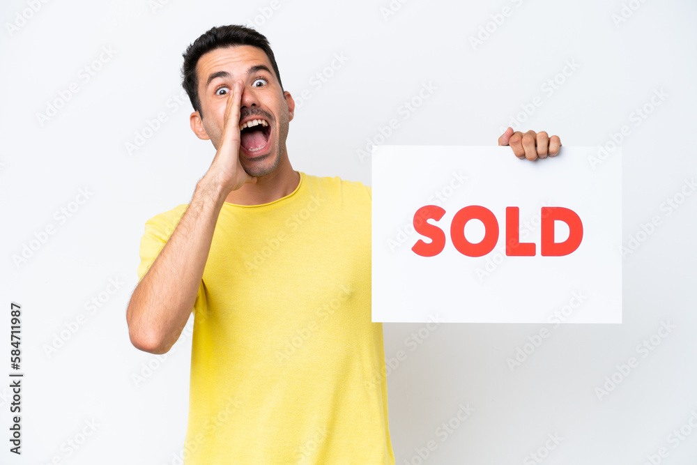 Young handsome man over isolated white background holding a placard with text SOLD and shouting Young handsome man over isolated white background holding a placard with text SOLD and shouting