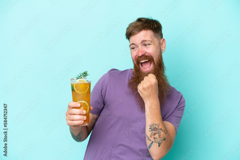Redhead man with long beard holding a cocktail isolated on blue background celebrating a victory Redhead man with long beard holding a cocktail isolated on blue background celebrating a victory
