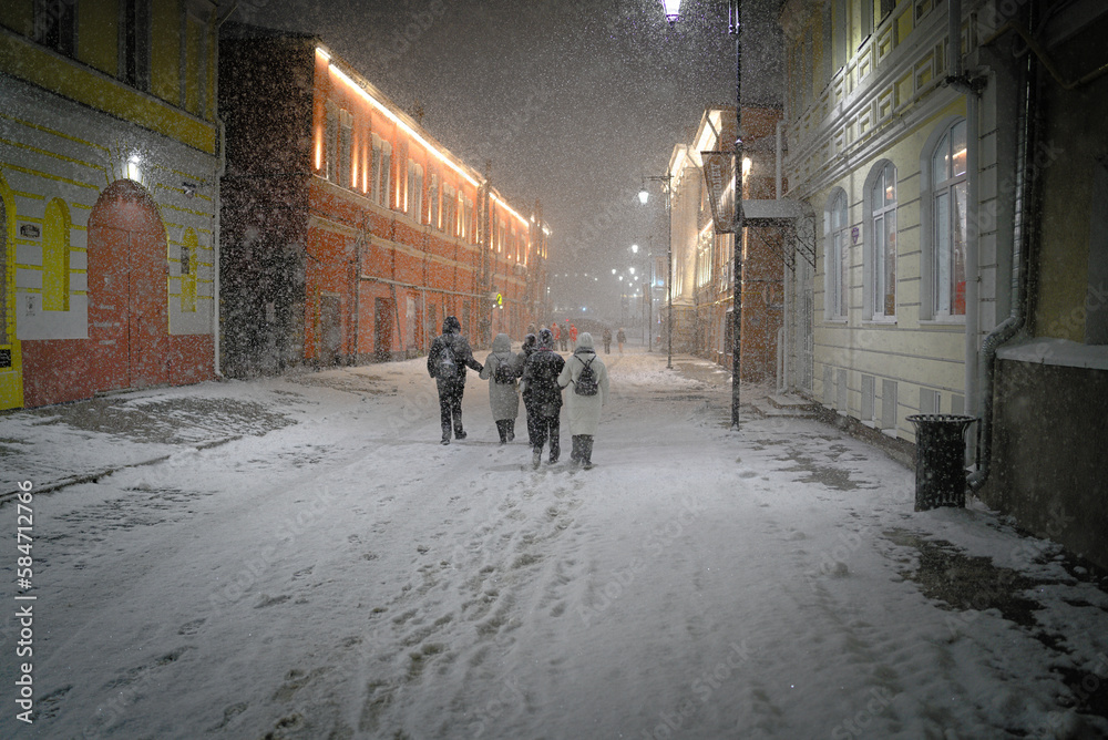 A snowstorm while walking along the ancient city streets. A group of people walking at night through the snow-covered city streets.