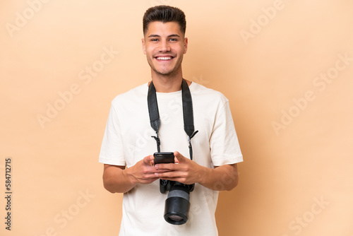 Young photographer caucasian man isolated on beige background sending a message with the mobile