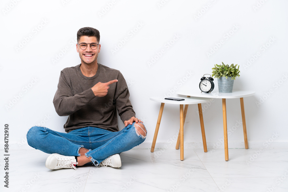 Young caucasian man sitting in his home isolated on white background pointing to the side to present a product Young caucasian man sitting in his home isolated on white background pointing to the side to present a product