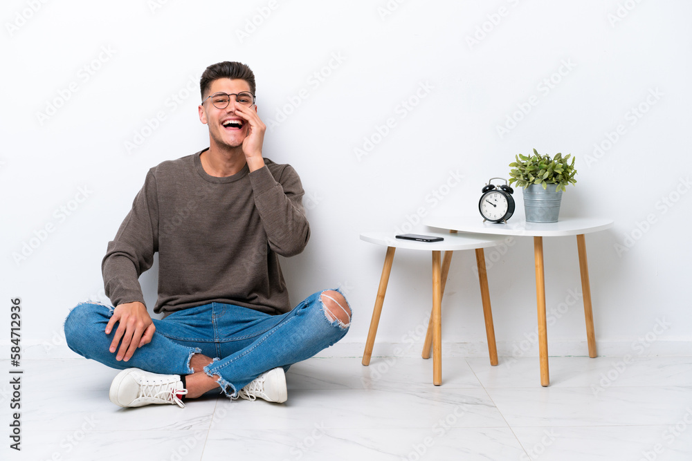 Young caucasian man sitting in his home isolated on white background shouting with mouth wide open Young caucasian man sitting in his home isolated on white background shouting with mouth wide open