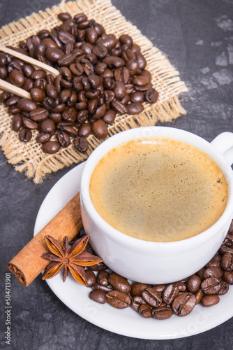 Coffee in white cup and roasted dark coffee beans with seasonings