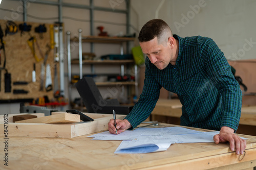 Portrait of a carpenter in a plaid shirt draws a workshop blueprint. 