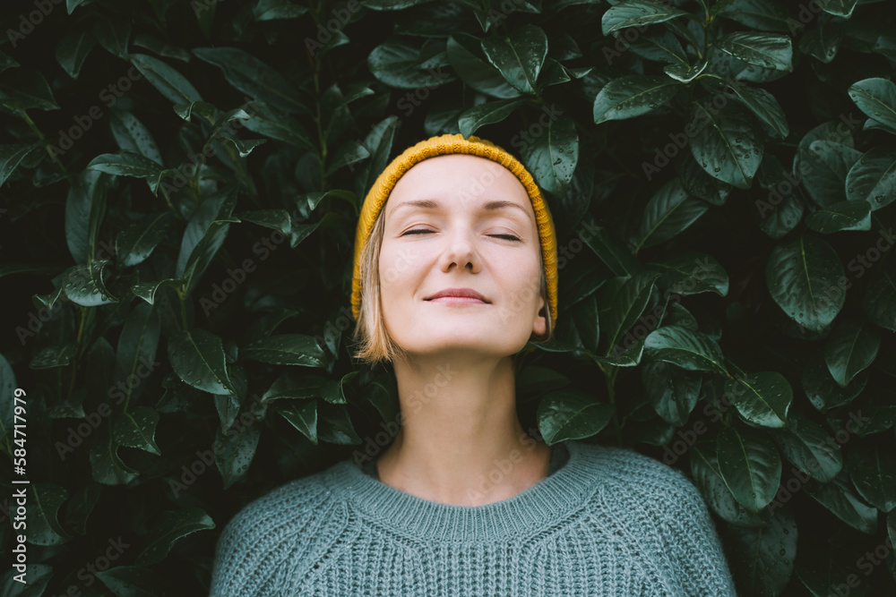 Portrait of relaxed and confident woman with eyes closed on background of green leaves wall. Thoughtful person in front of green hedge. Joy, zen and balance people. Stability through mental health - obrazy, fototapety, plakaty 