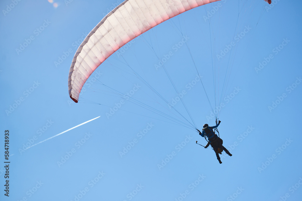 Skydiver on blue paraglider in blue sky. and a white trail from the plane in the sky Skydiver on blue paraglider in blue sky. and a white trail from the plane in the sky