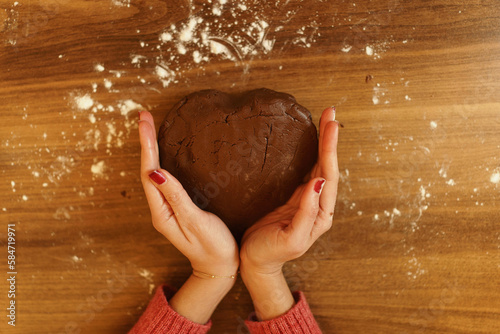 Close-up image of dough kneaded in heart shape and framed by hands. A visual evoking the love of making pastries, cakes and cookies and cooking for your loved ones.