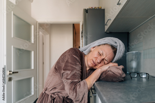 Mature woman in velvet bathrobe and towel on head feeling bad. hangover or feeling sick concept, hard sleepy morning 
