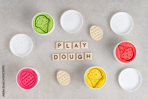 Colorful dough in white jars on gray background. PLAY DOUGH written with tile letters. Flat lay