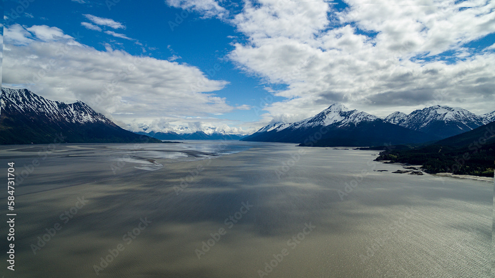 Aerial view of a snowy mountain range covered with clouds against a lake in Hope, Alaska