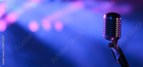 Vintage vocal microphone in the dark on a concert stage with pink and blue spot lighting. Live music or podcast wide banner background with copy space