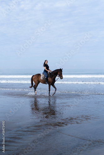 Young woman riding a horse on the beach at the ocean. © Yuliya Kirayonak