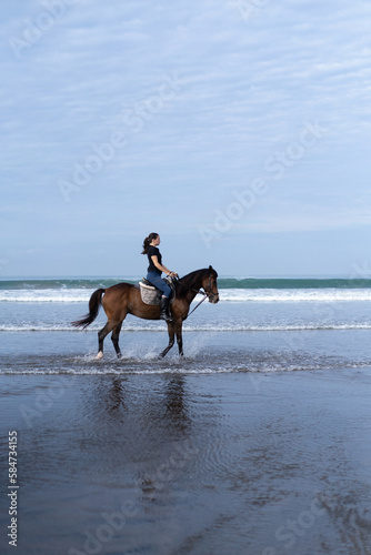 Young woman riding a horse on the beach at the ocean.