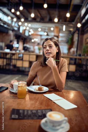 Young woman in her thoughts sitting in coffee shop, having cake and coffee.