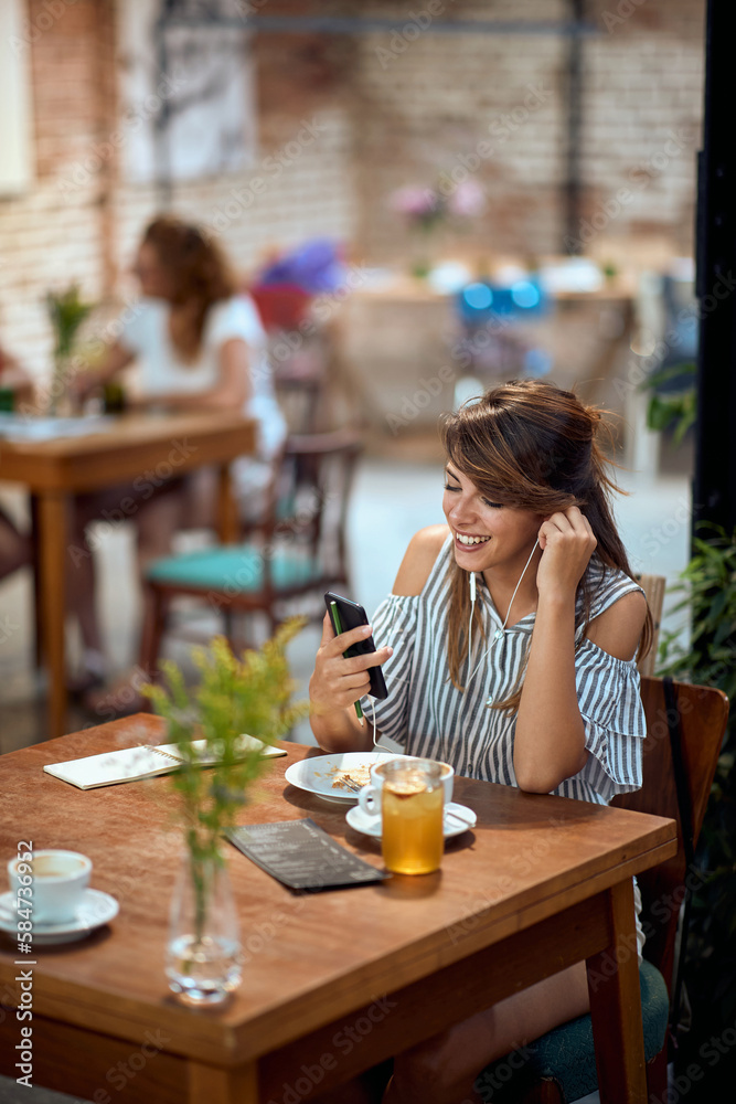 Beautiful smiling young woman with earphones at cafe having a video call. Beautiful smiling young woman with earphones at cafe having a video call.