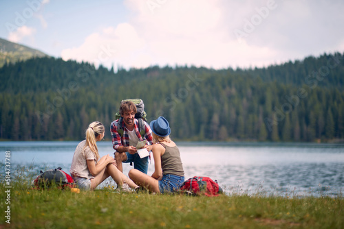 A group of friends is chatting beside the lake during hiking the hills. Trip, nature, hiking