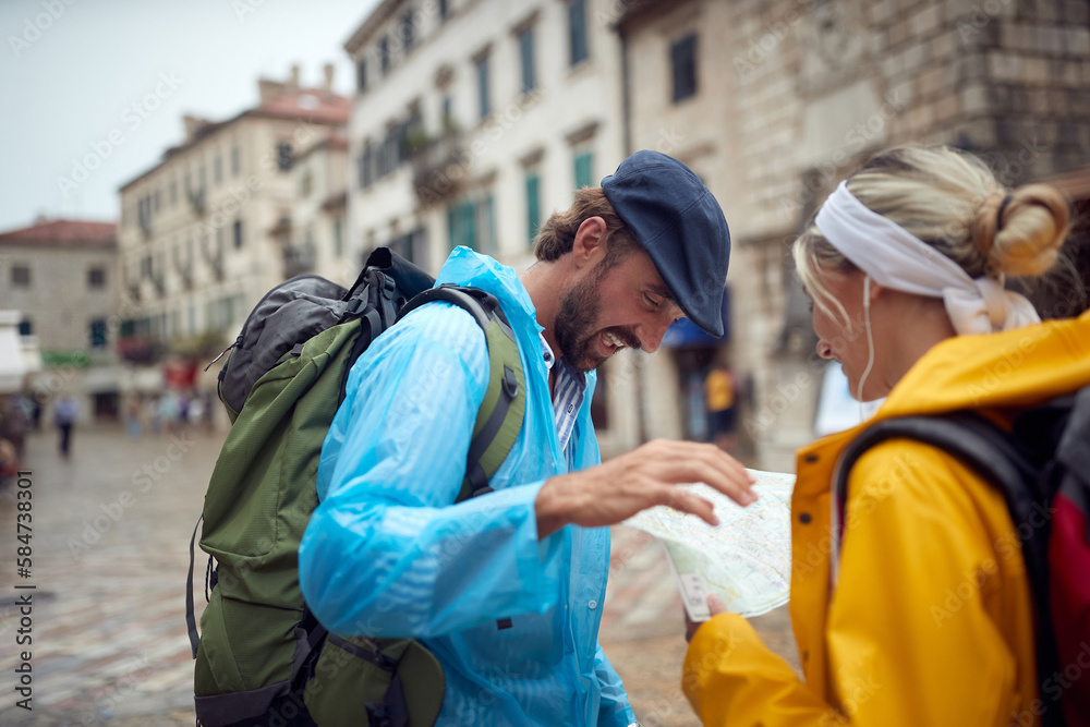 Navigating through new city, couple in raincoats on walk. Joyful man and woman on holiday. Travel, togetherness, city, lifestyle concept. Navigating through new city, couple in raincoats on walk. Joyful man and woman on holiday. Travel, togetherness, city, lifestyle concept.
