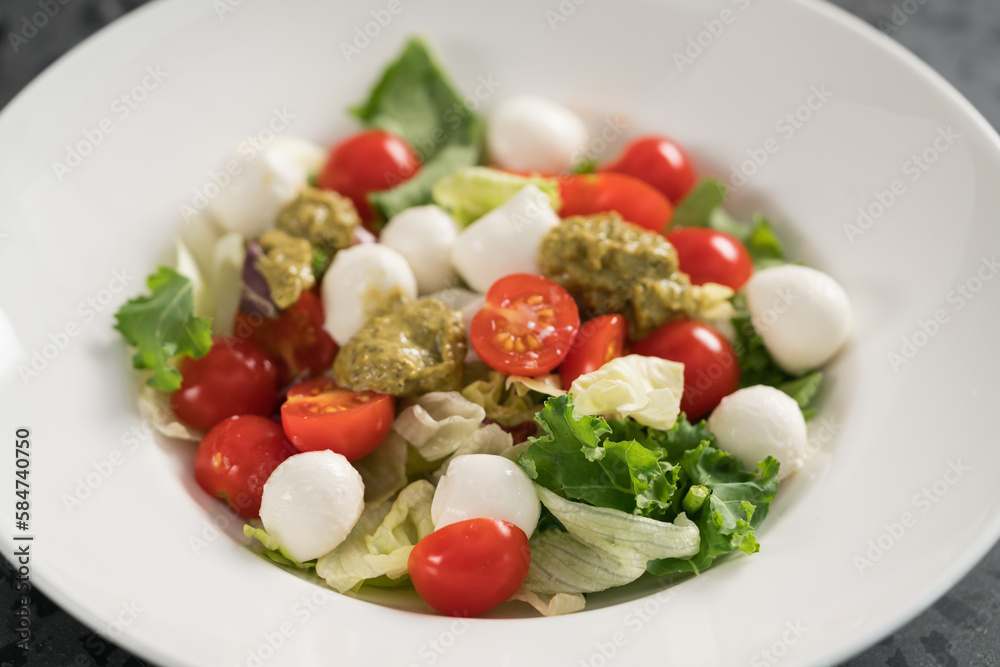 Salad with miced greens , tomatoes and mozzarella in white bowl