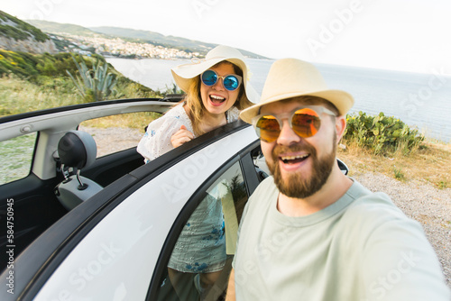 Romantic couple making selfie on smartphone camera in rental cabrio car on ocean or sea beach enjoying summer vacation together and taking picture on cellular resting near sea on weekends © satura_