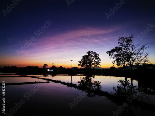 Beutiful Twilight sky over the silhouette trees beside the pond in the rice fields unseen in Thailand