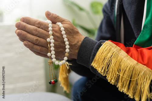 an elderly man prays with a rosary and the flag of the United Arab Emirates photo