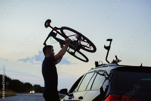 A man mounts his bicycle on the roof of a car at sunset. The concept of outdoor recreation..