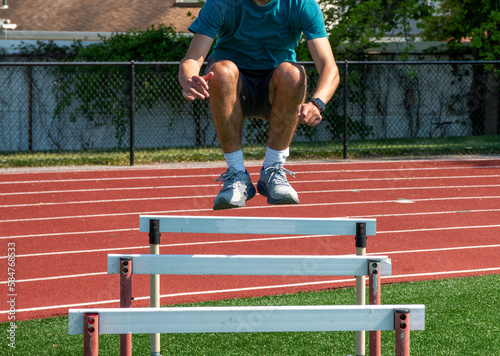 Teenage boy jumping over track hurdles for agility and strength