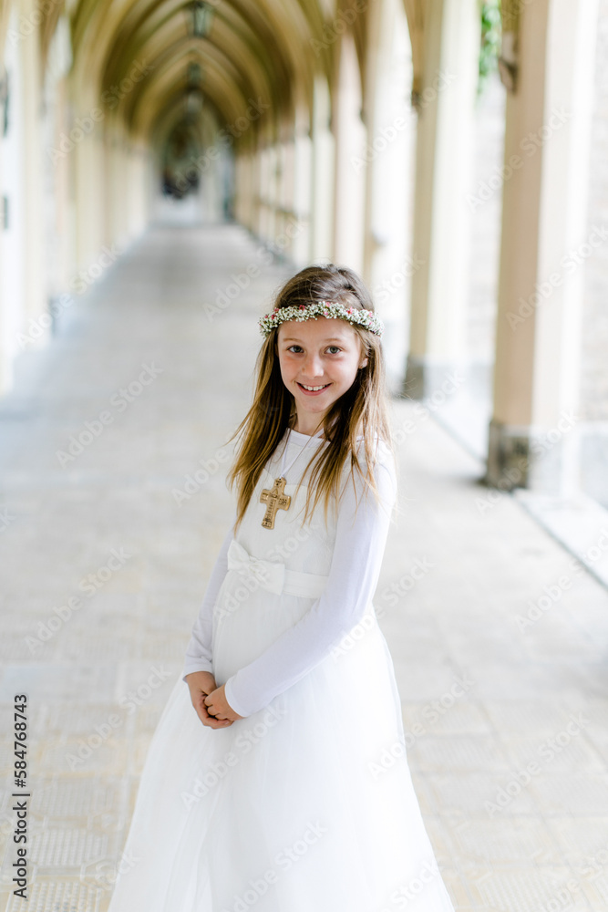 Hübsches junges Mädchen im weißen Kleid mit Blumenkranz bei Erstkommunion