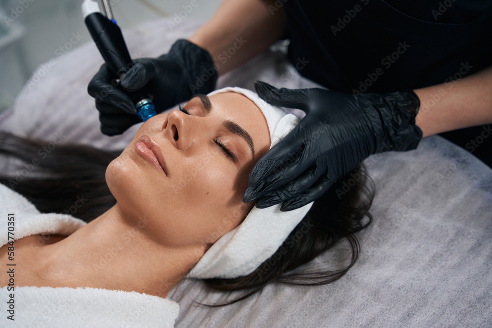 Beautician doing facial skin rejuvenation for beautiful client
