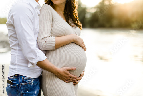 Mutter und Vater halten Babybauch während Sonnenuntergang photo