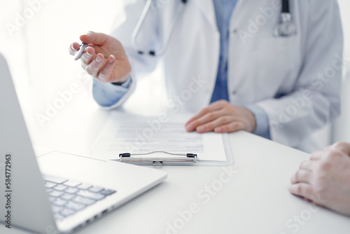 Doctor and patient sitting at the table in clinic office. The focus is on female physician s hand pointing to laptop computer monitor  close up. Medicine concept