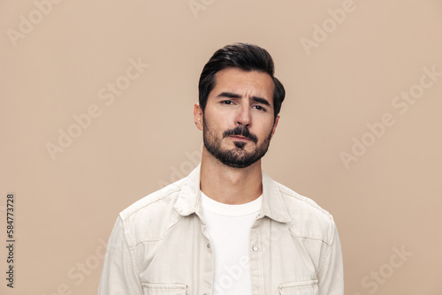 Portrait of a stylish man dissatisfied and angry screaming on a beige background in a white t-shirt looking at the camera, fashionable clothing style, copy space, space for text © SHOTPRIME STUDIO