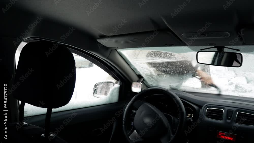 Driver outside cleans the frozen windshield of the car in winter cold snowy weather Driver outside cleans the frozen windshield of the car in winter cold snowy weather