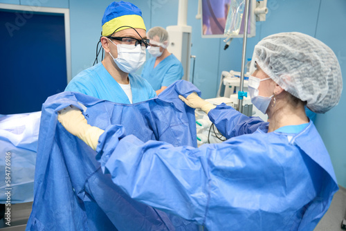 Foto Nurse helps the doctor to put on a sterile gown