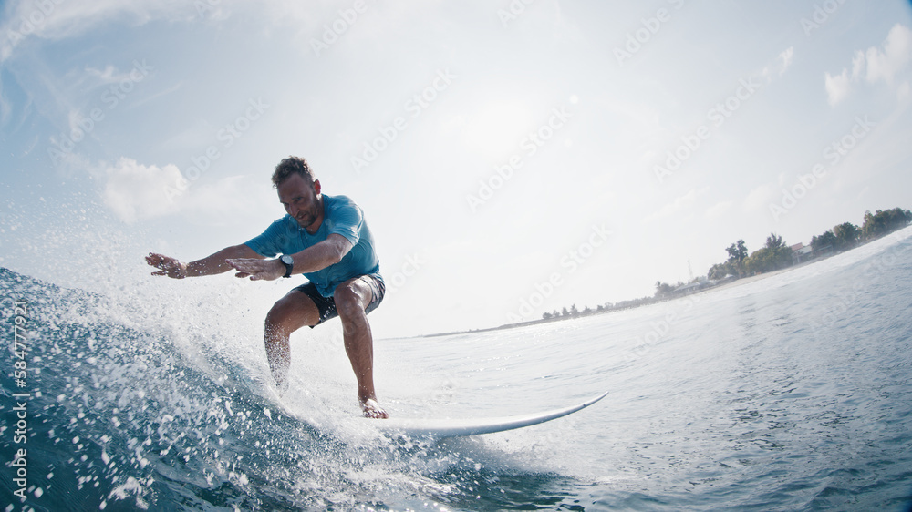 Surfer rides the wave. Young man surfs the ocean wave in the Maldives and looks into the camera Surfer rides the wave. Young man surfs the ocean wave in the Maldives and looks into the camera