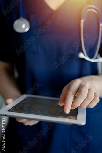 Doctor woman using tablet computer while standing near panorama window in clinic, close up. Physician or surgeon at work. Medicine concept photo